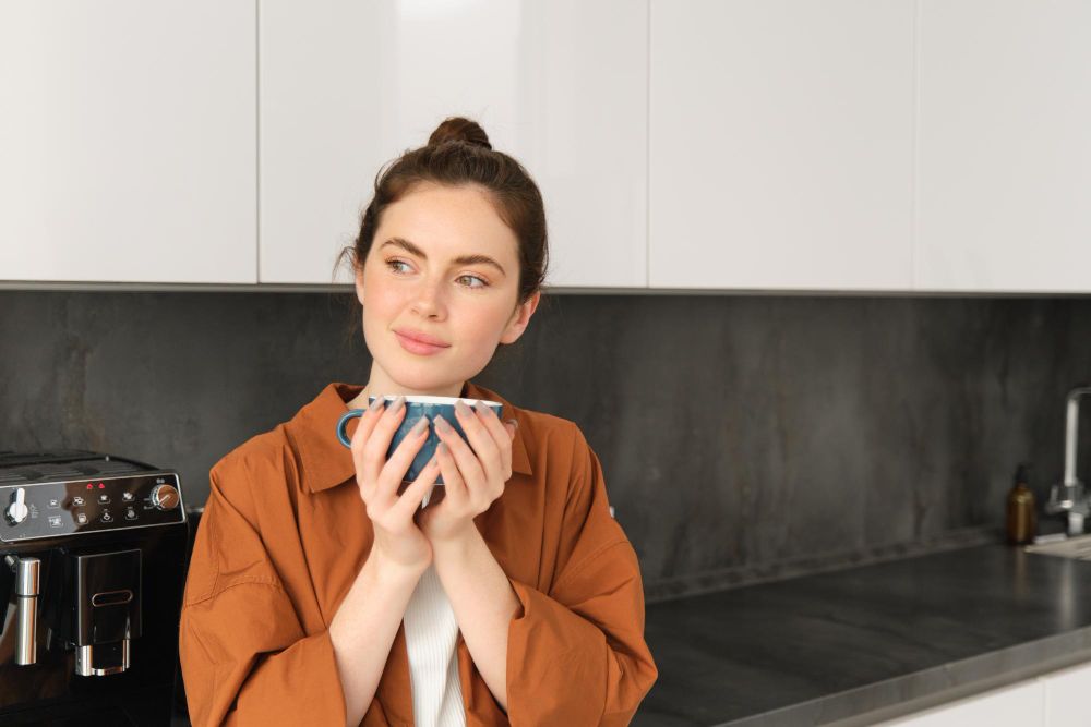 Mujer disfrutando una taza de café junto a una cafetera en una cocina moderna