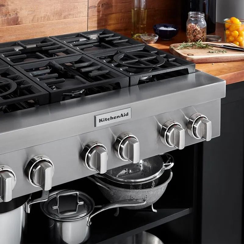 Estufa de empotrar a gas KitchenAid con seis quemadores y utensilios de cocina.