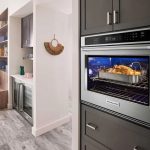 Pollo sazonado en bandeja de acero dentro de un horno eléctrico empotrado en cocina contemporánea