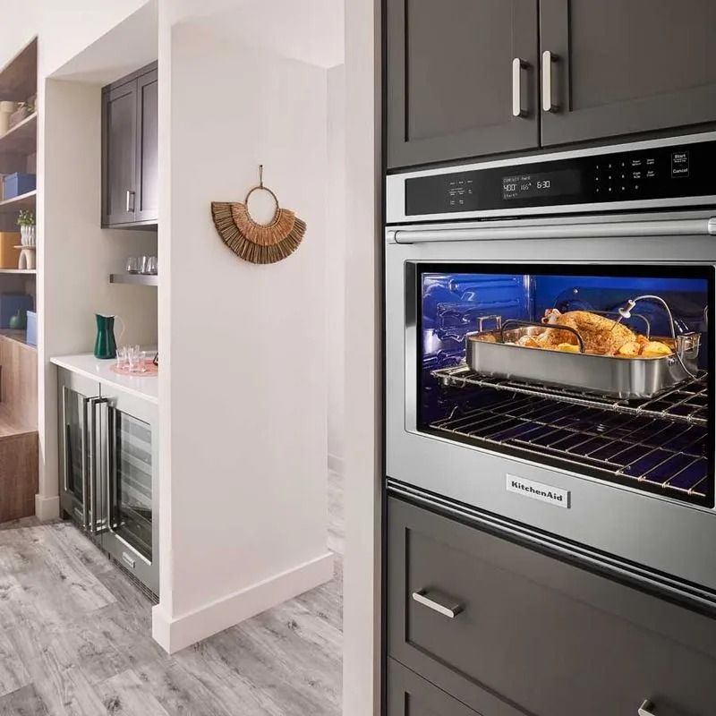 Pollo sazonado en bandeja de acero dentro de un horno eléctrico empotrado en cocina contemporánea