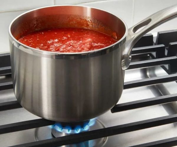 Estufa de empotrar a gas con sartén de acero inoxidable y salsa en cocción.